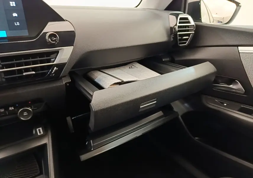 Intérieur de la Citroën C4 X noir, vue côté passager avec boîte à gants ouverte et tableau de bord moderne.