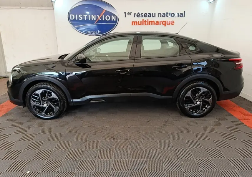 Profil côté gauche de la Citroën C4 X noire 2023 avec jantes noires et lignes fluides, en intérieur showroom.