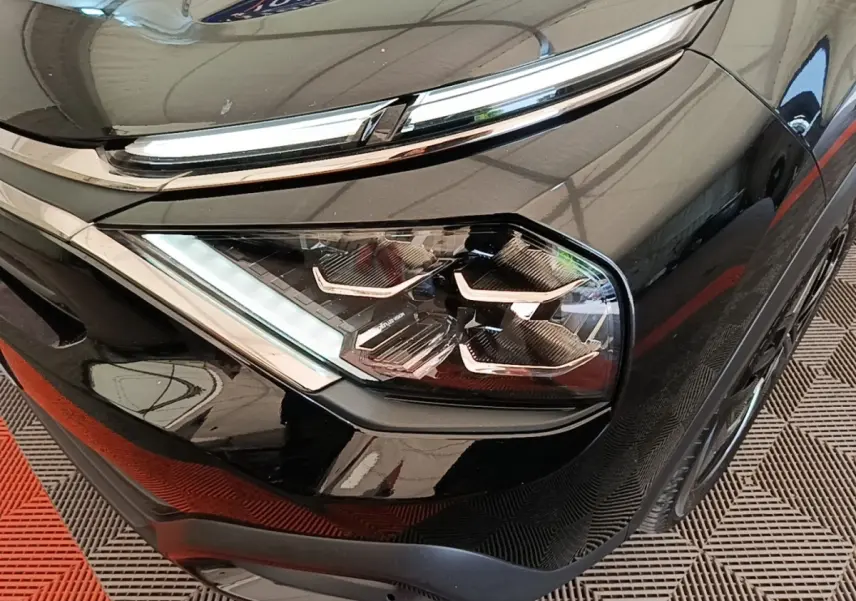 Gros plan sur le phare avant droit noir brillant de la Citroën C4 X 2023 avec détails LED et chrome autour.
