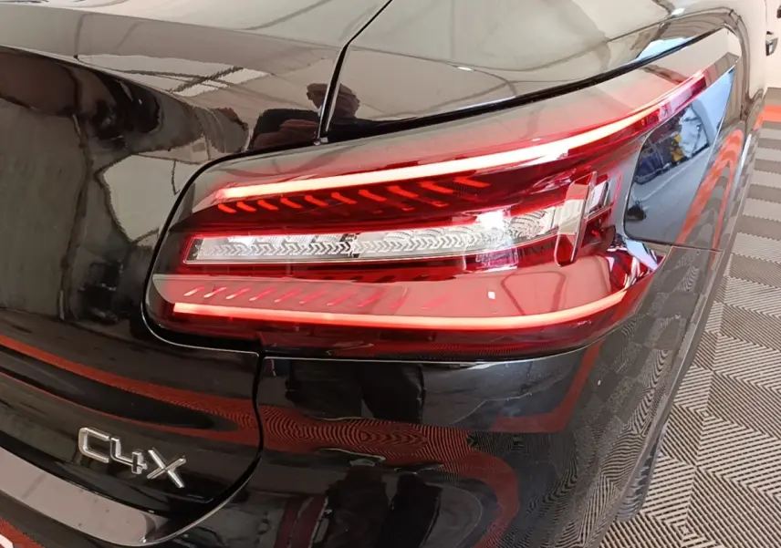 Gros plan sur le feu arrière droit rouge et blanc d'une Citroën C4 X noire avec logo C4 X visible sur la malle arrière.