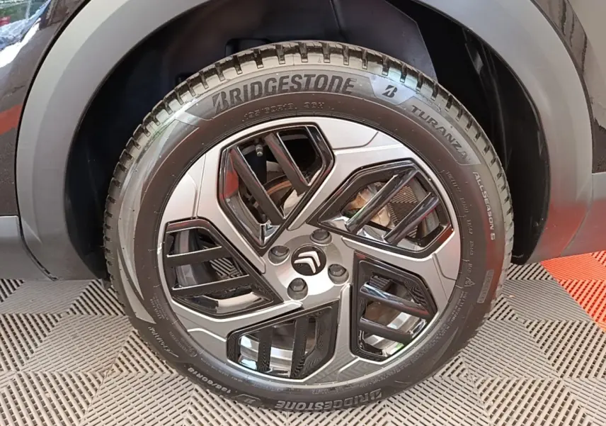 Gros plan sur la roue avant droite noire d'une Citroën C4 X 2023 avec jante alliage au design géométrique.