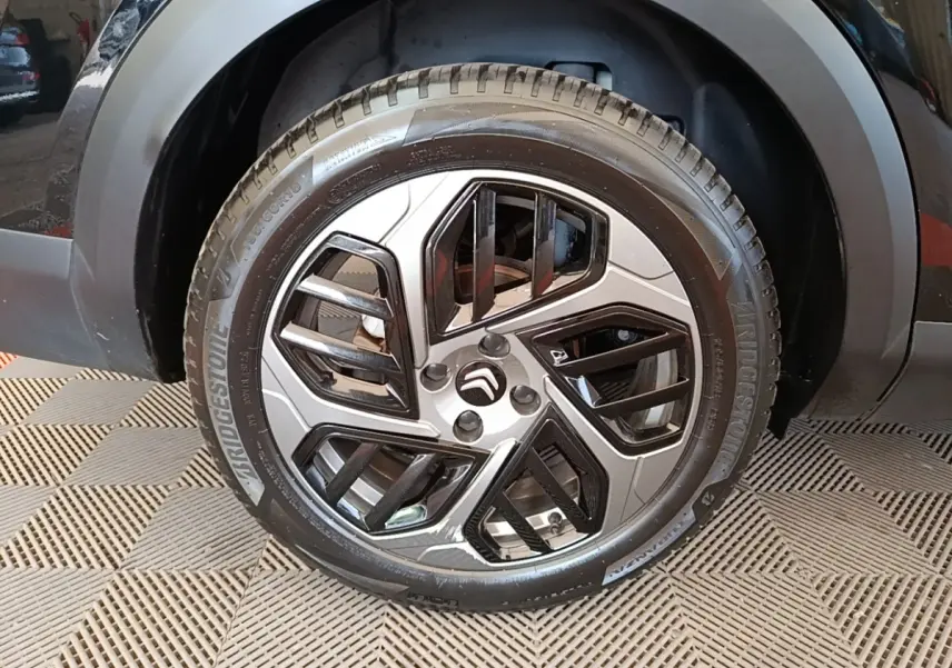 Gros plan sur la roue avant droite noire d'une Citroën C4 X 2023 avec jante alliage au design géométrique.