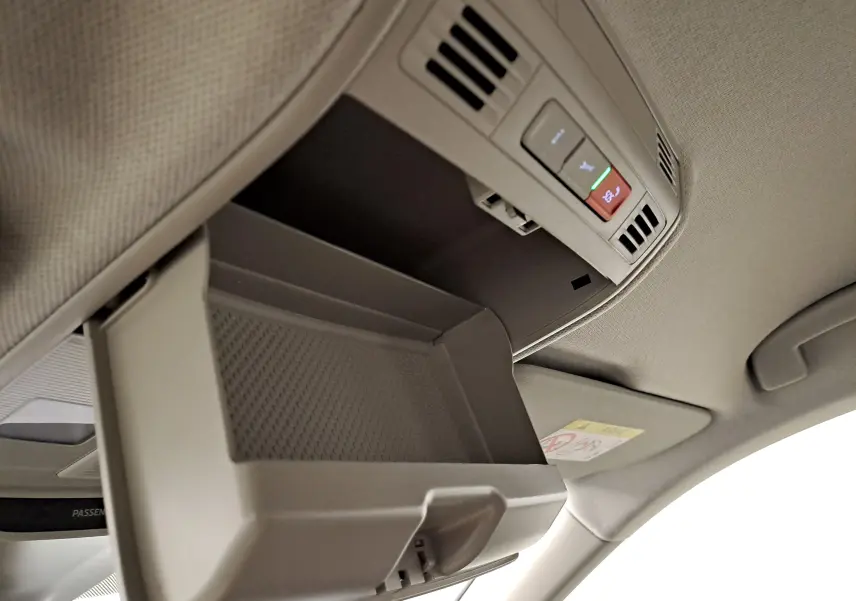 Vue intérieure en plongée du rangement lunettes ouvert sur le plafond du Skoda Kamiq blanc Lune, avec commandes d'éclairage intégrées.