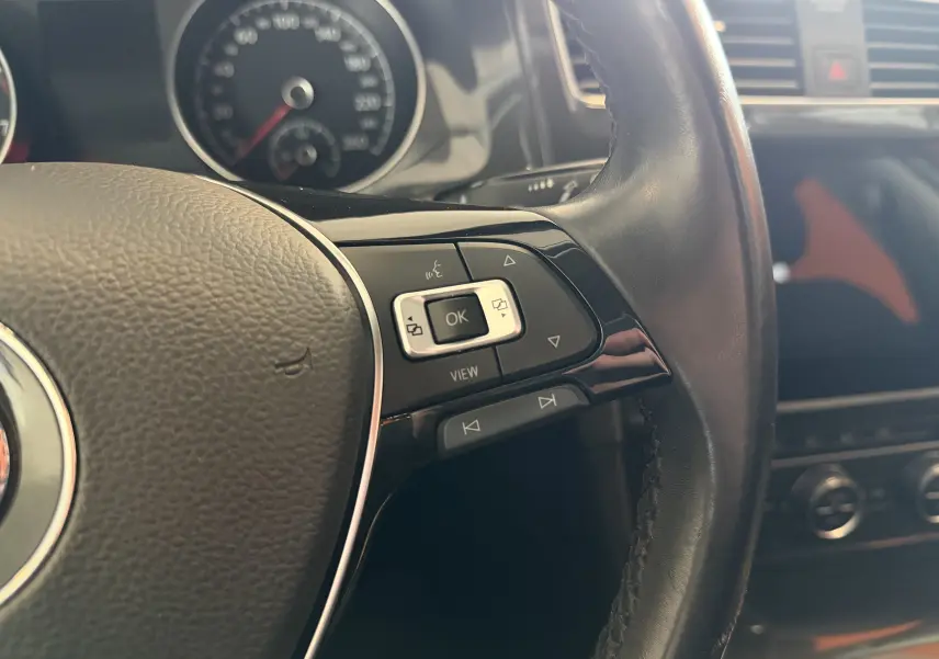 Gros plan sur le volant noir de la Volkswagen Golf TSI 130 Confortline 2019, avec commandes multifonctions et tableau de bord flou.