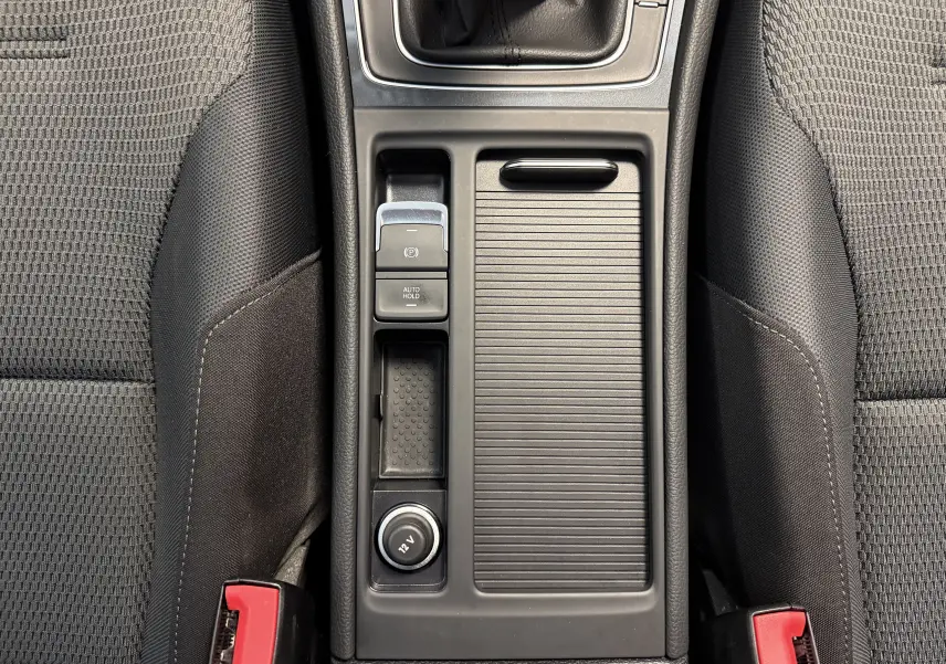 Vue plongeante sur la console centrale noire de la Volkswagen Golf TSI 130 Confortline avec frein à main électrique et prise 12V.