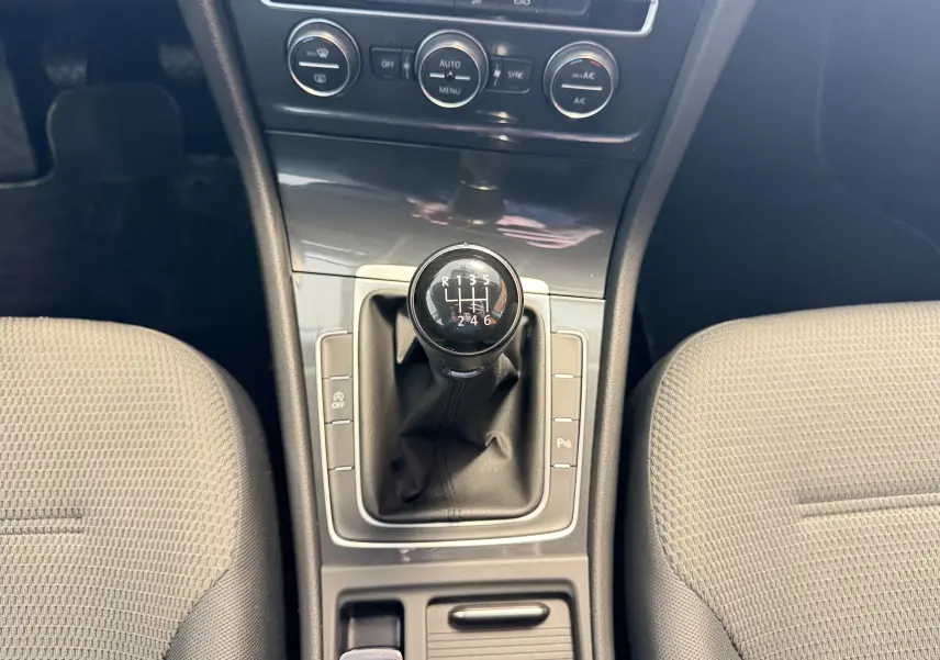 Vue intérieure centrée sur le levier de vitesses manuel de la Volkswagen Golf TSI 130 Confortline gris, entouré des sièges avant.