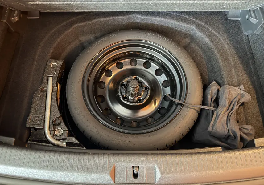Vue plongeante sur la roue de secours noire et les outils dans le coffre d'une Volkswagen Golf TSI 130 Confortline gris.