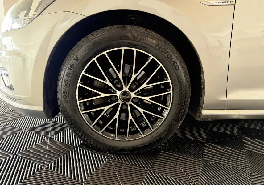 Gros plan sur la roue avant gauche d'une Volkswagen Golf gris clair avec jante alliage noir et argent et badge Bluemotion sur l'aile.