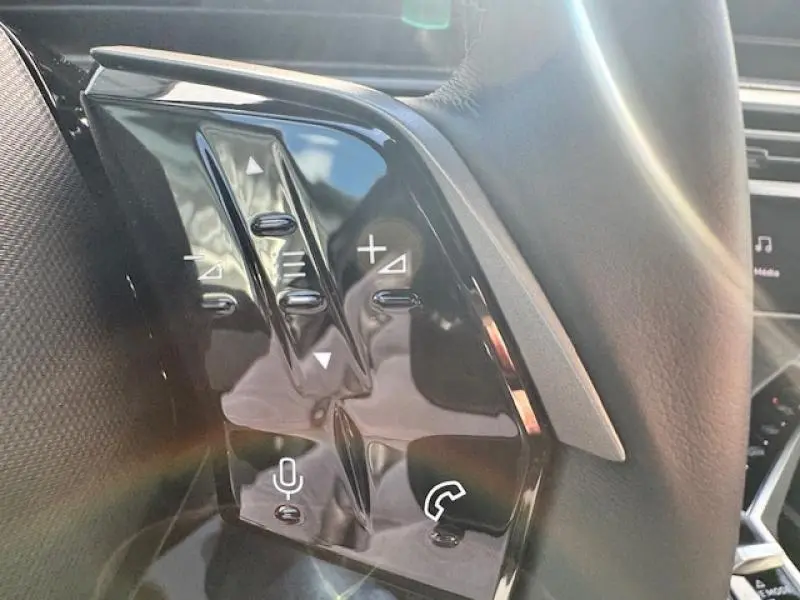 Gros plan sur les commandes au volant noir brillant du Peugeot 5008 Hybrid 2025, avec boutons volume et appel.