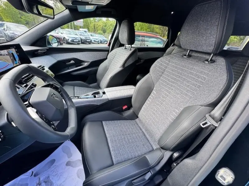 Vue intérieure côté conducteur du Peugeot 5008 Hybrid 2025 avec sièges tissu gris et cuir noir, volant multifonction cuir.