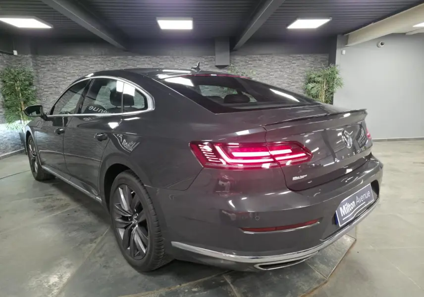 Volkswagen Arteon gris 3/4 arrière droit en intérieur, feux arrière LED allumés et jantes alliage 18 pouces.