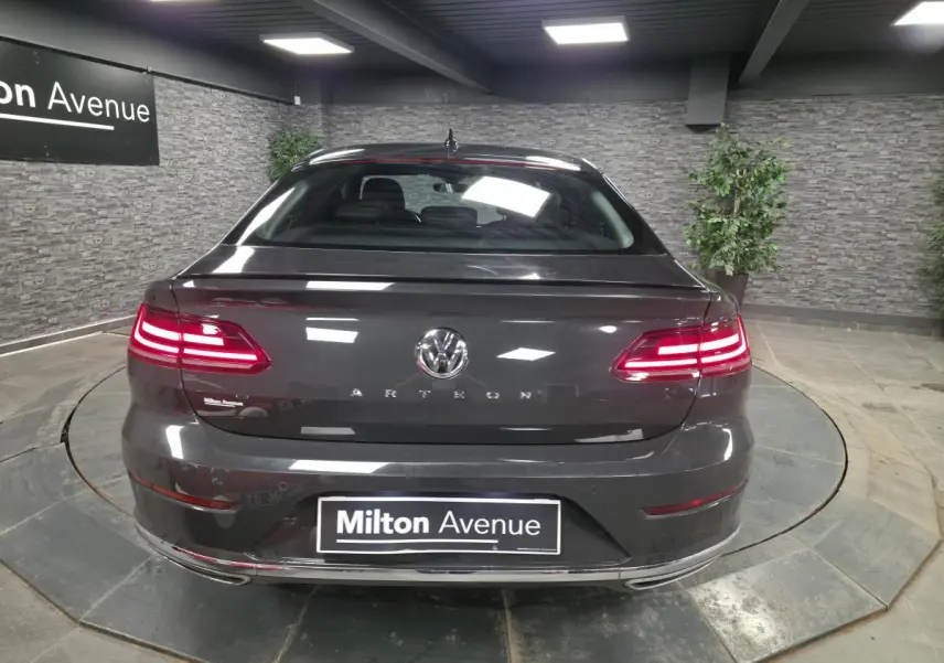 Vue arrière d’une Volkswagen Arteon gris Urano avec feux LED allumés et badge R-Line visible en intérieur showroom.