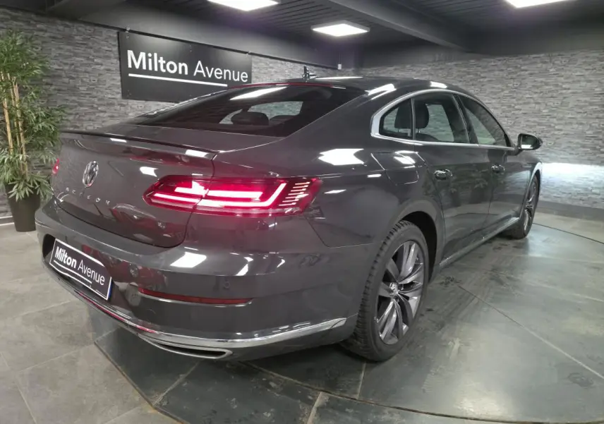 Volkswagen Arteon gris 3/4 arrière droit avec feux LED allumés et jantes alliage 18 pouces en showroom.