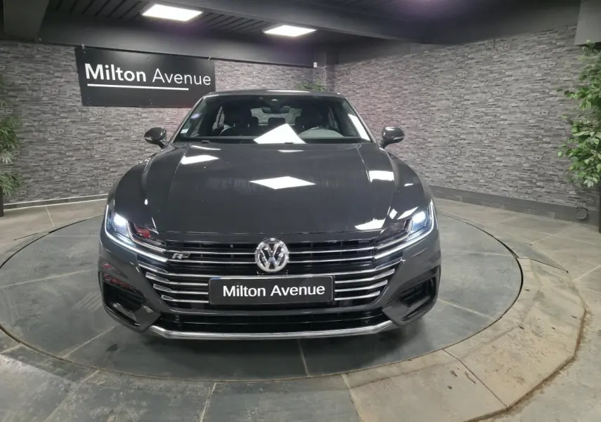 Vue avant d'une Volkswagen Arteon gris Urano avec calandre chromée et phares LED allumés dans un showroom.