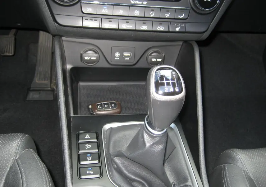 Vue rapprochée de la console centrale noire du Hyundai Tucson 2016, mettant en valeur le levier de vitesse manuel et les commandes adjacentes.