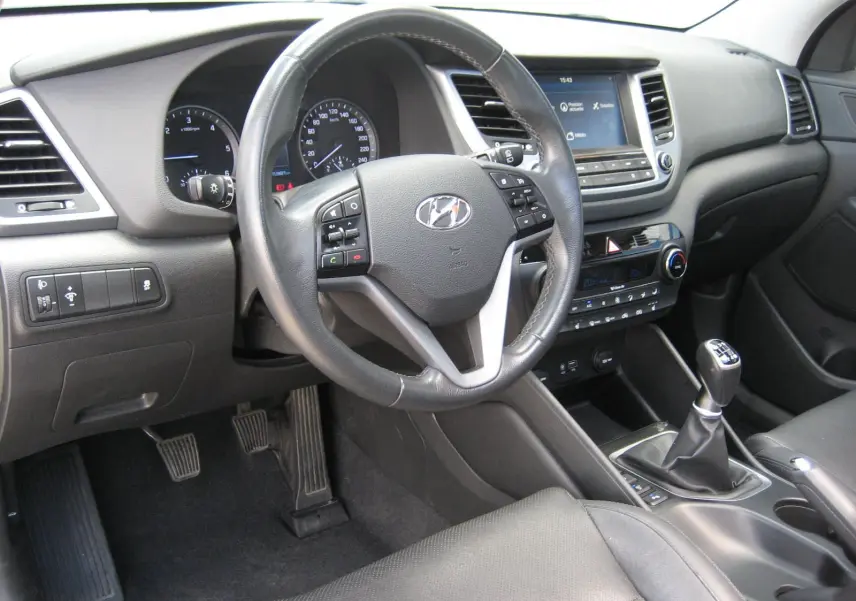 Intérieur du Hyundai Tucson 2016 vu côté conducteur, volant cuir multifonction et tableau de bord avec écran tactile.