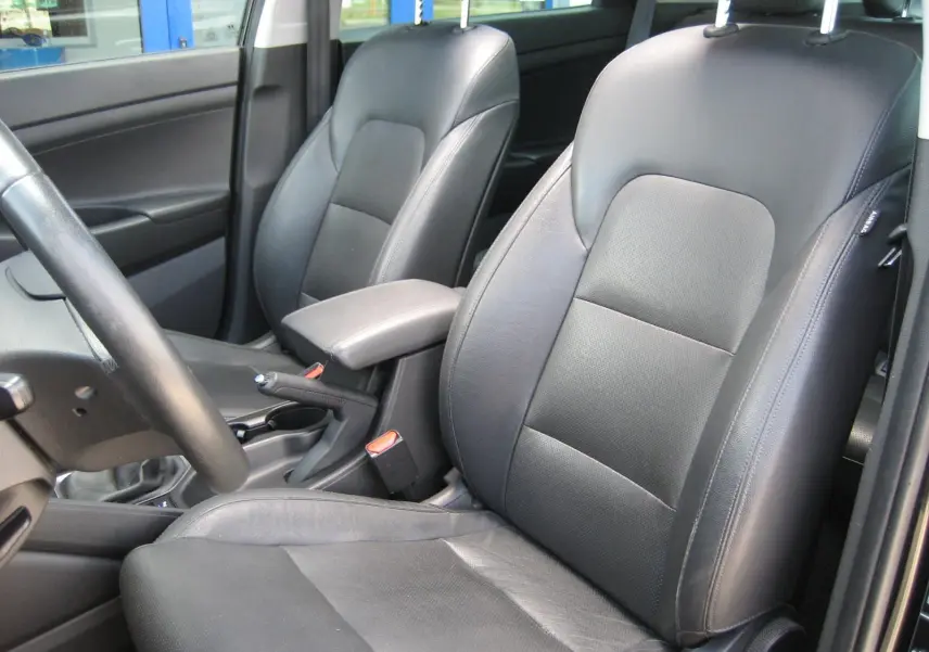 Vue intérieure côté avant droit du Hyundai Tucson 2016, sièges en cuir noir et accoudoir central visible.