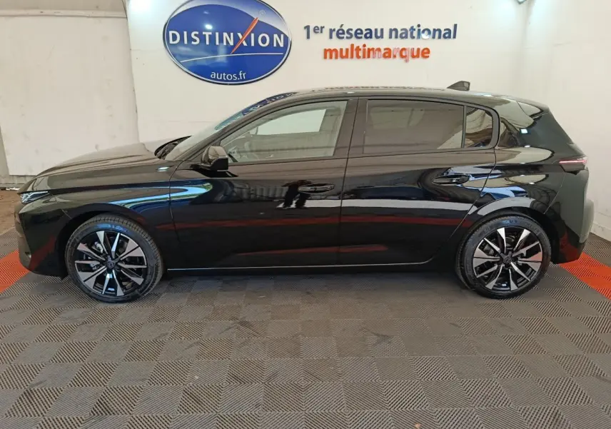 Profil côté gauche de la Peugeot 308 noire 2026 avec jantes alliage bicolores et vitres teintées, en intérieur showroom.