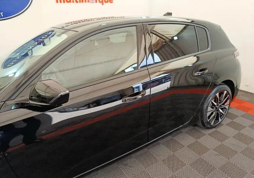 Vue latérale droite d'une Peugeot 308 noire 2026 avec jantes alliage et vitres teintées, sur sol damier intérieur.
