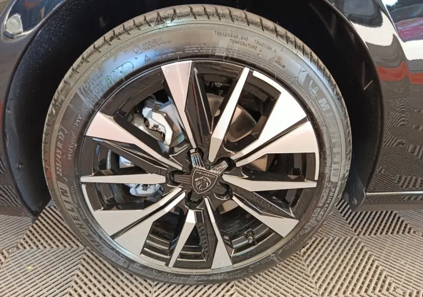 Gros plan sur la roue avant droite noire avec jante alliage bicolore et logo Peugeot au centre.