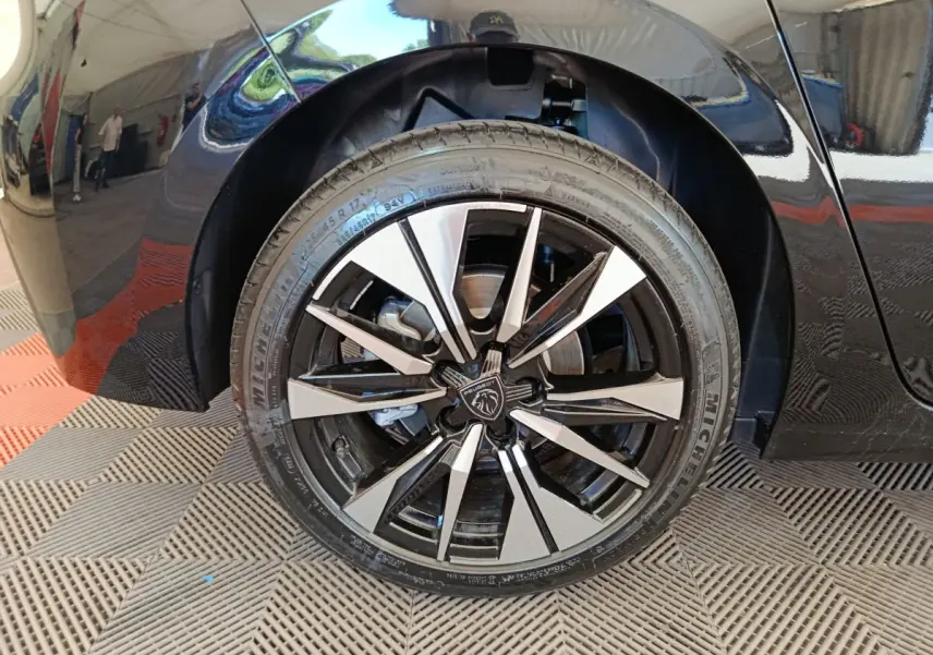Gros plan sur la roue avant droite noire d’une Peugeot 308 2026 avec jante alliage bicolore et logo central lion.