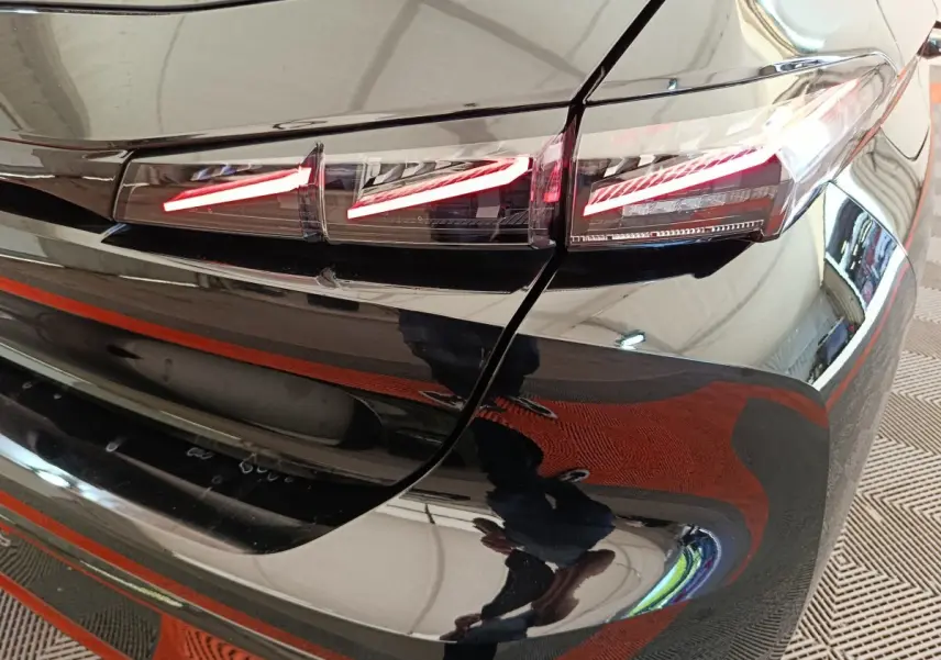 Gros plan sur le feu arrière droit rouge allumé d'une Peugeot 308 noire, reflet brillant sur la carrosserie.