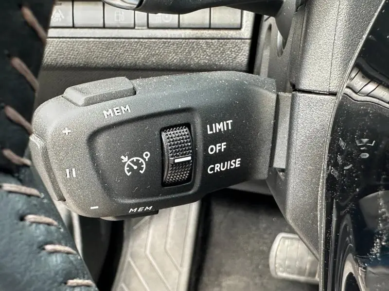 Gros plan sur la commande de régulateur de vitesse du Peugeot 3008 Hybride Rechargeable noir Perla Nera, côté gauche du volant.
