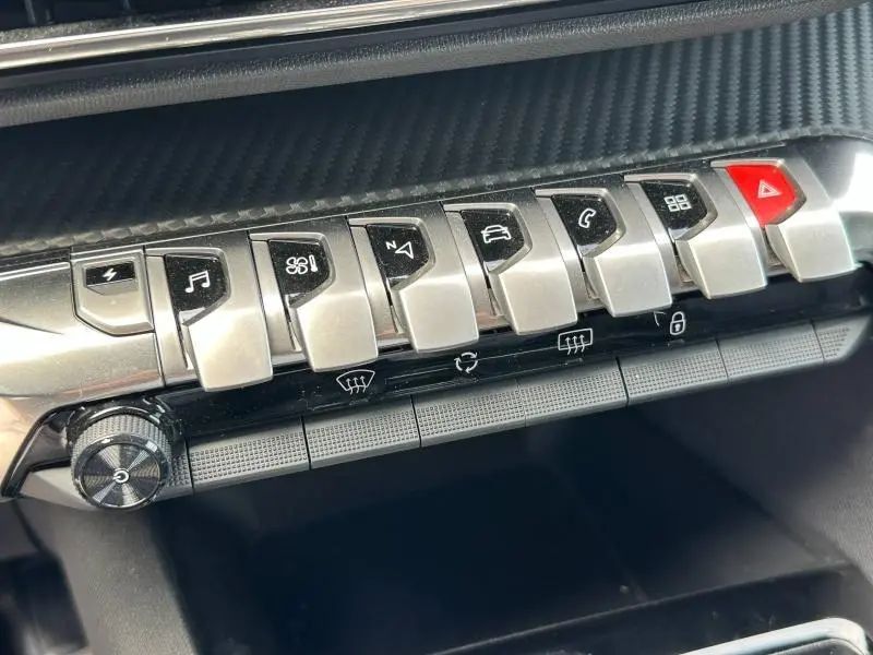 Gros plan sur la rangée de boutons argentés et noirs de la console centrale du Peugeot 3008 Hybride 2024, avec finition carbone.