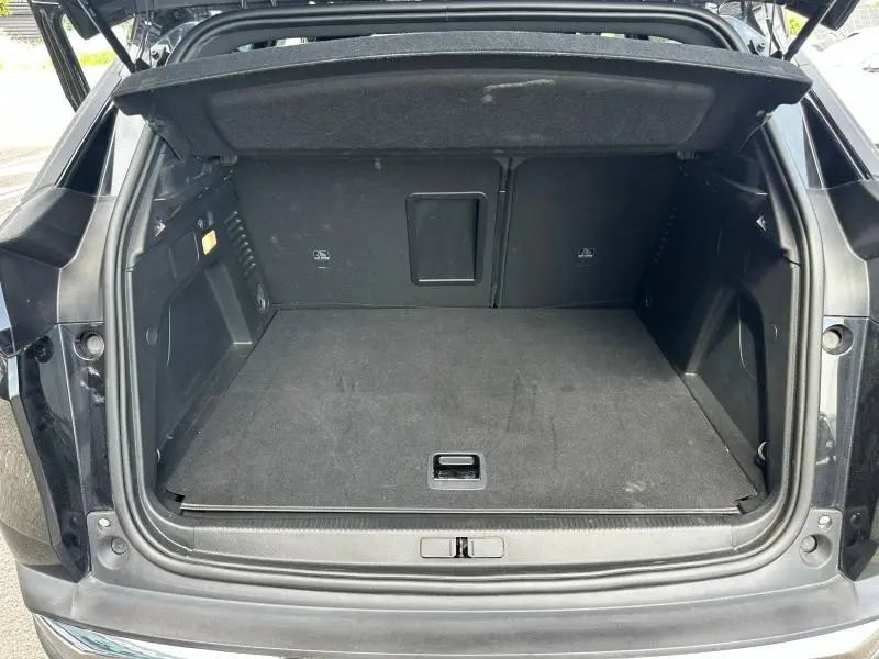 Coffre ouvert vu de l'arrière d'un Peugeot 3008 Hybride Rechargeable noir Perla Nera, espace de chargement vide et tapis noir.