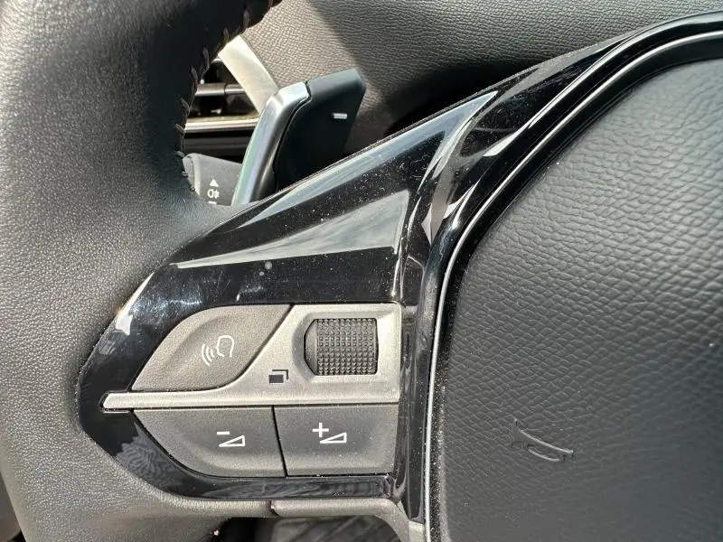 Gros plan sur les commandes gauche du volant cuir noir du Peugeot 3008 Hybride Rechargeable 2024, avec molette et boutons.
