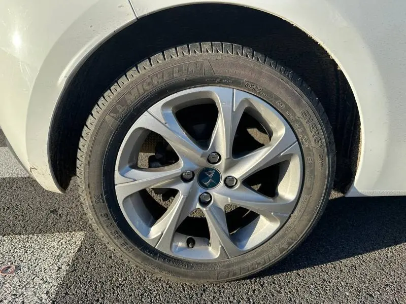 Gros plan sur la roue arrière droite d'une DS3 blanche avec jante alliage 5 branches et logo DS au centre.