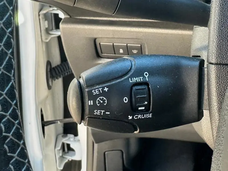 Gros plan sur la commande de régulateur de vitesse noire à gauche du volant dans une DS3 noire de 2016.