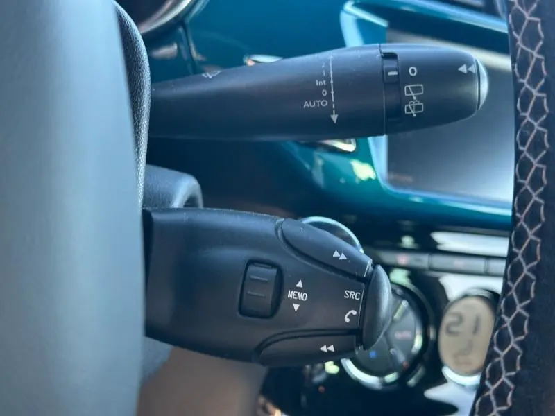 Gros plan sur les commandes au volant noir d'une DS3 2016, avec tableau de bord bleu et climatisation digitale en arrière-plan.