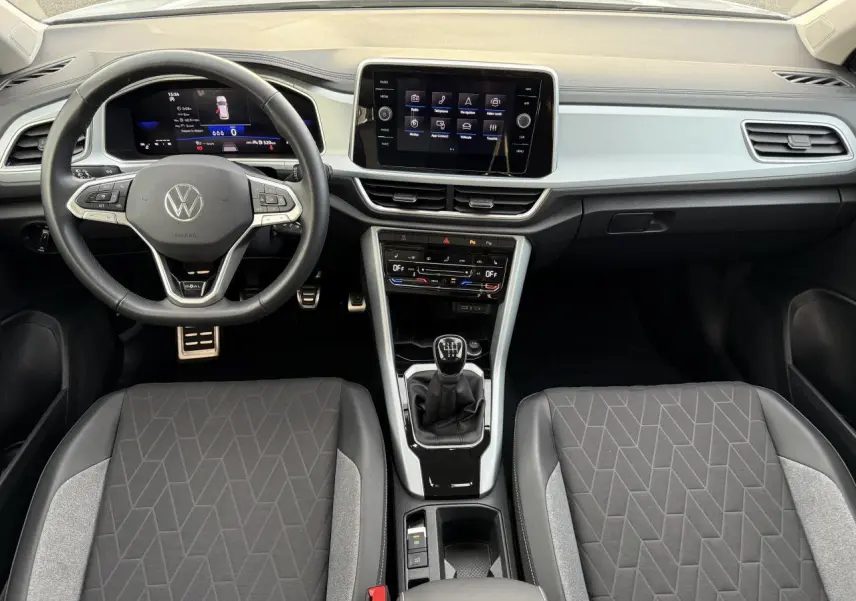 Intérieur du Volkswagen T-Roc 2025 vu de face, tableau de bord moderne avec écran tactile et volant cuir multifonction.