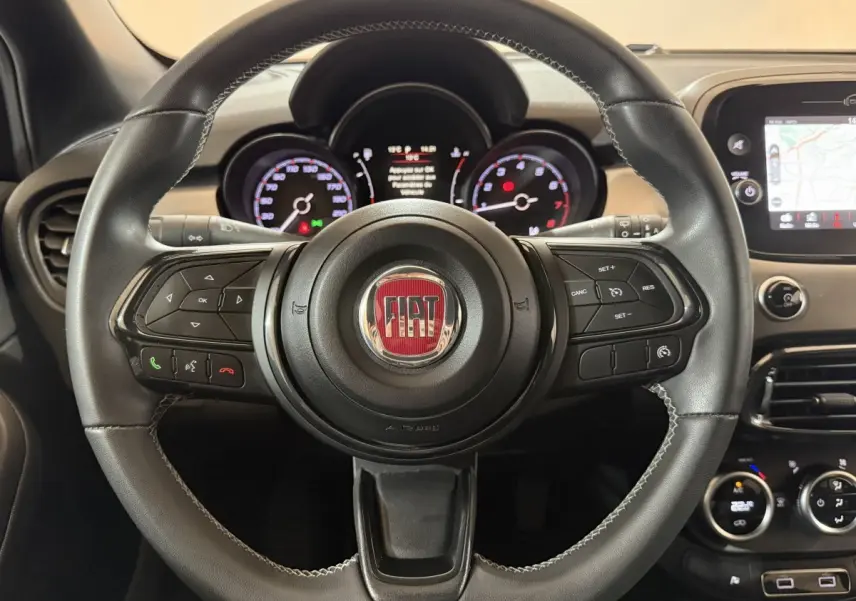 Volant cuir noir de Fiat 500X 2021 avec commandes multifonctions et tableau de bord numérique en arrière-plan.