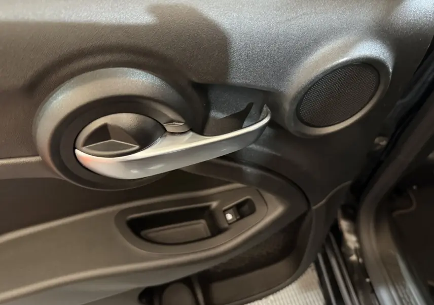 Poignée intérieure de porte côté gauche noire avec haut-parleur rond sur Fiat 500X noir, vue rapprochée depuis l'intérieur.