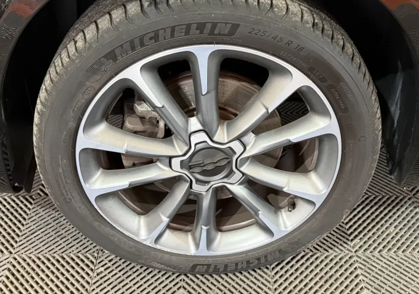 Gros plan sur la jante alliage argentée avec logo Fiat au centre, montée sur pneu Michelin du Fiat 500X noir.