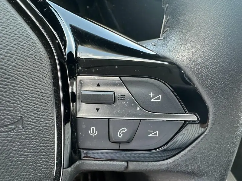 Gros plan sur les commandes multifonctions noires du volant du Peugeot 308 2024, avec boutons de volume et téléphone.