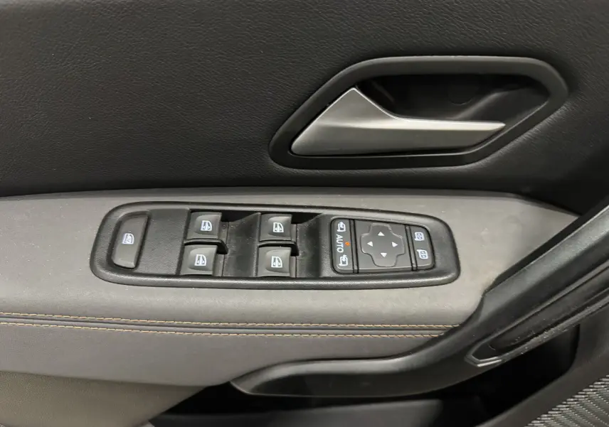 Gros plan sur la commande des vitres électriques et la poignée intérieure côté gauche du Dacia Duster 2024, finition tissu gris.