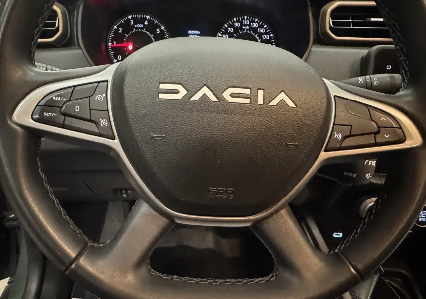 Vue rapprochée du volant noir du Dacia Duster 2024 avec commandes intégrées et tableau de bord partiellement visible.