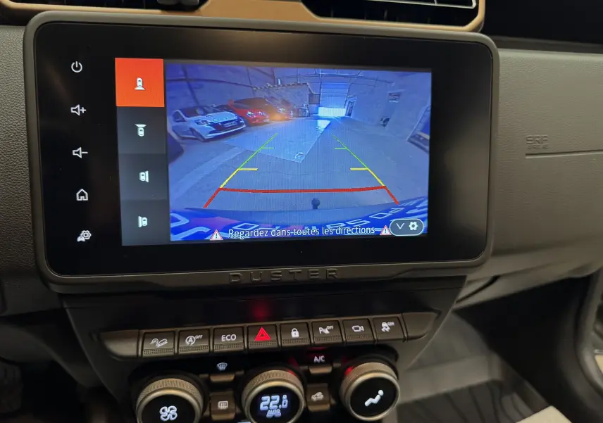 Écran tactile intérieur du Dacia Duster 2024 montrant la caméra de recul avec vue arrière sur un parking.