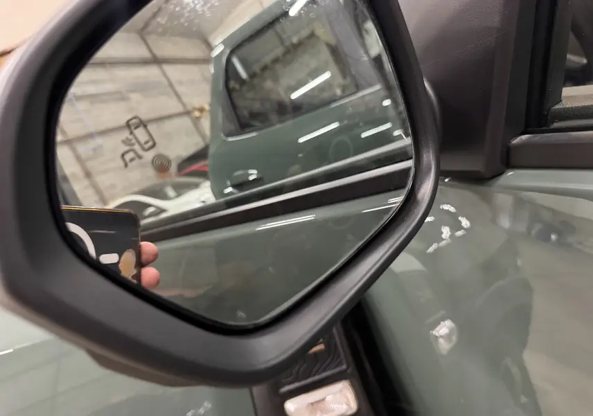 Rétroviseur côté gauche d’un Dacia Duster 2024 kaki lichen, avec reflet de la portière et du cadre intérieur noir.
