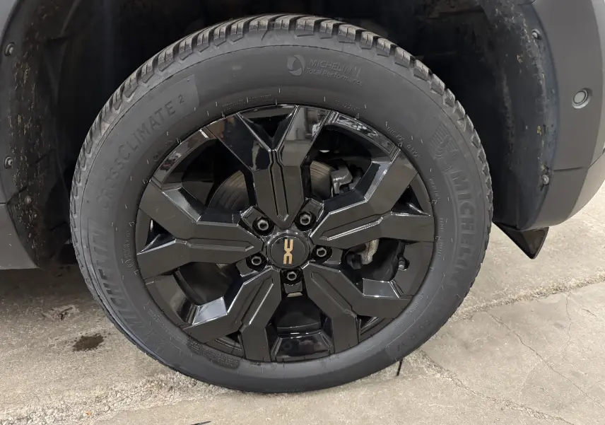 Gros plan sur la roue avant droite du Dacia Duster 2024 kaki lichen, jante noire brillante avec logo Duster central.