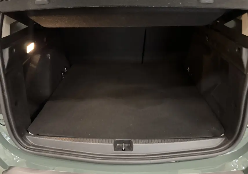 Coffre ouvert vu de l'arrière d'un Dacia Duster 2024 kaki lichen, espace de chargement vide et éclairé à gauche.