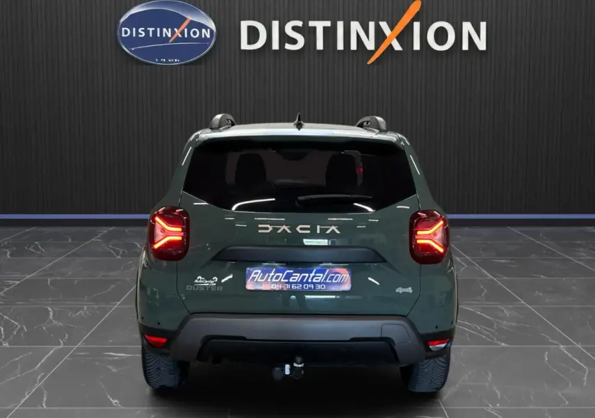 Vue arrière d'un Dacia Duster 2024 kaki lichen avec feux LED allumés et attelage visible en intérieur showroom.