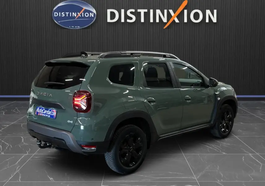 Vue 3/4 arrière droite du Dacia Duster 2024 kaki lichen avec jantes noires et attelage visible en intérieur showroom.