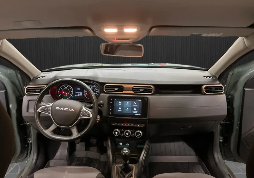 Vue intérieure frontale du Dacia Duster 2024 kaki lichen, mettant en valeur le tableau de bord et la console centrale avec écran tactile.