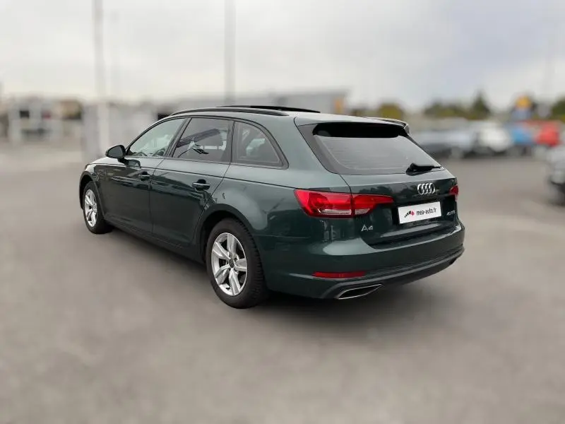 Audi A4 Avant vert vue 3/4 arrière droit, avec vitres surteintées et jantes alu visibles sur parking flou.