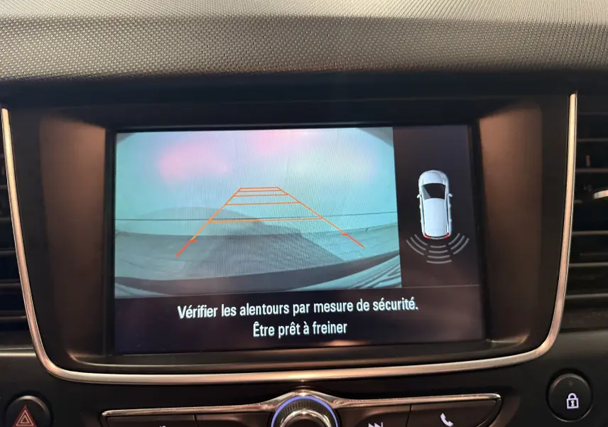 Écran intérieur de l’Opel Crossland gris 2023 montrant la caméra de recul avec lignes de guidage et alertes de sécurité.