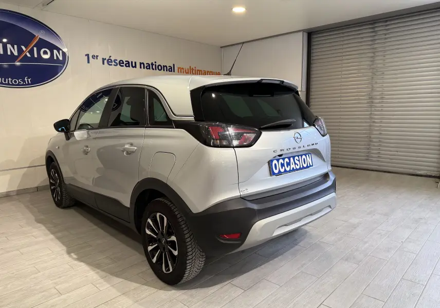 Vue 3/4 arrière droite d’un Opel Crossland gris 2023 avec toit noir et jantes alliage, en intérieur showroom.